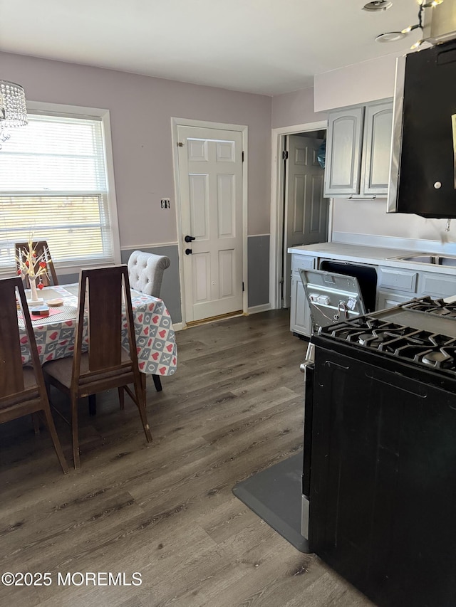 kitchen featuring black range with gas cooktop, a sink, wood finished floors, light countertops, and gray cabinets