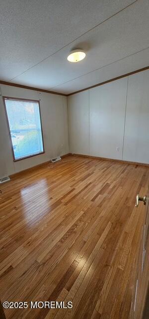 empty room featuring ornamental molding, wood-type flooring, and a textured ceiling