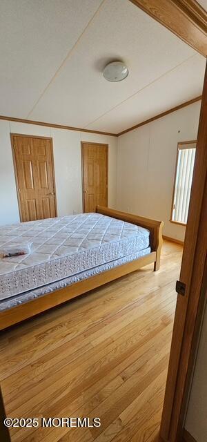 unfurnished bedroom with wood-type flooring, vaulted ceiling, and ornamental molding