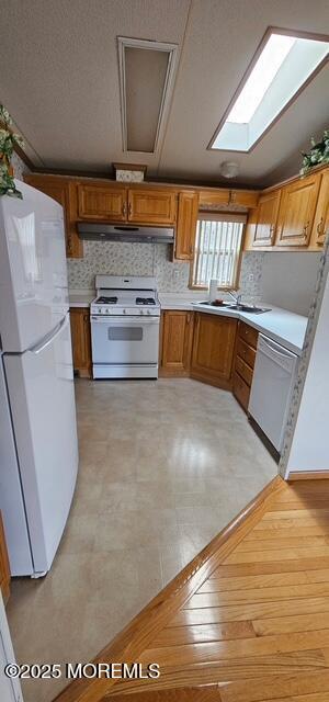 kitchen featuring sink, white appliances, a skylight, and backsplash