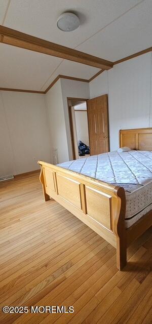 unfurnished bedroom featuring ornamental molding, vaulted ceiling, and light hardwood / wood-style flooring