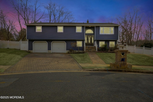 split foyer home featuring a garage, a front lawn, decorative driveway, and fence