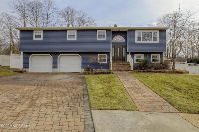 bi-level home with a garage, fence, decorative driveway, and a front yard