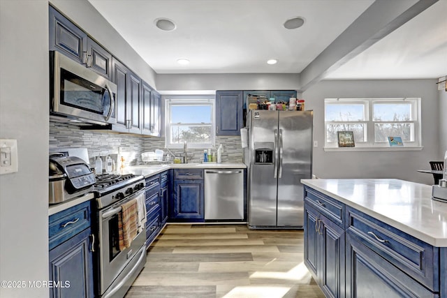 kitchen with blue cabinets, appliances with stainless steel finishes, light countertops, and backsplash