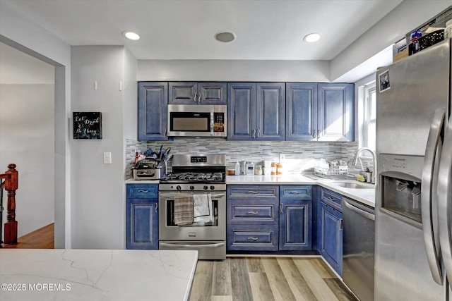 kitchen featuring tasteful backsplash, light wood-style floors, stainless steel appliances, blue cabinetry, and a sink