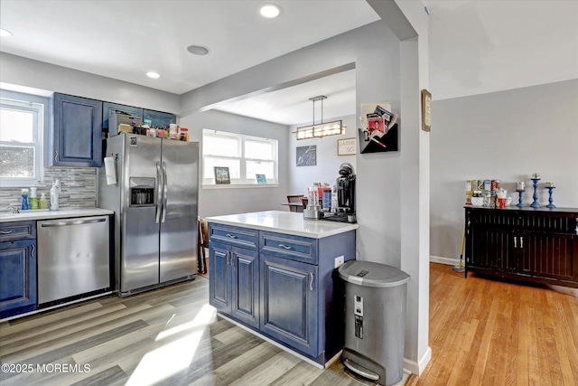 kitchen with appliances with stainless steel finishes, decorative light fixtures, light countertops, blue cabinetry, and backsplash