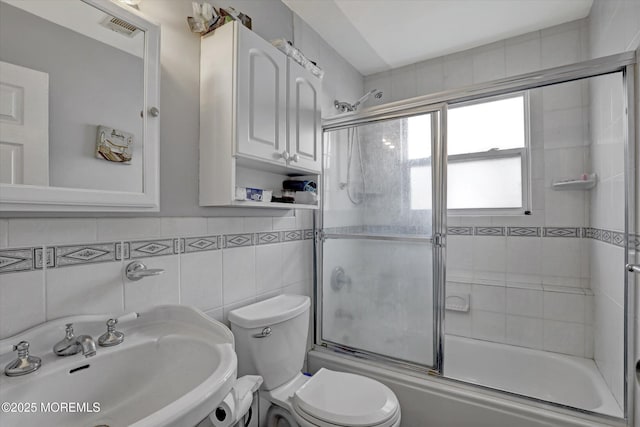 full bathroom featuring visible vents, toilet, shower / bath combination with glass door, a sink, and tile walls