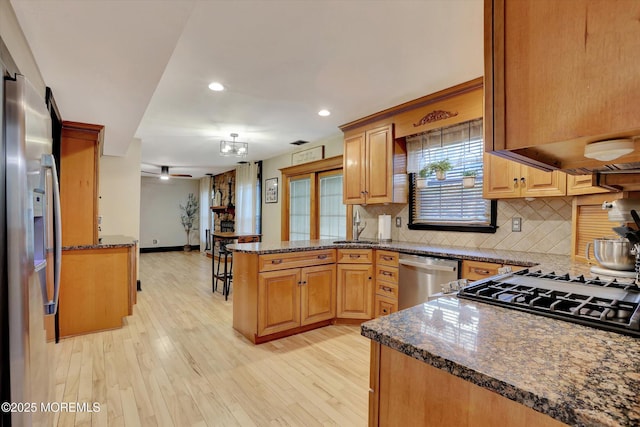 kitchen featuring backsplash, stainless steel appliances, light hardwood / wood-style floors, kitchen peninsula, and dark stone counters