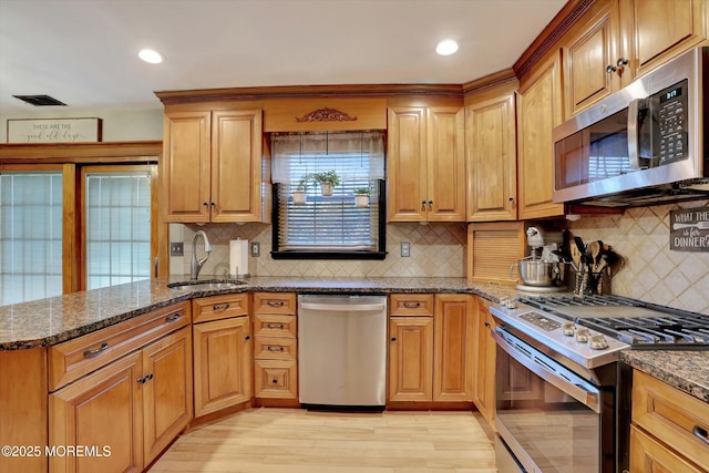 kitchen featuring sink, decorative backsplash, dark stone counters, light hardwood / wood-style floors, and stainless steel appliances