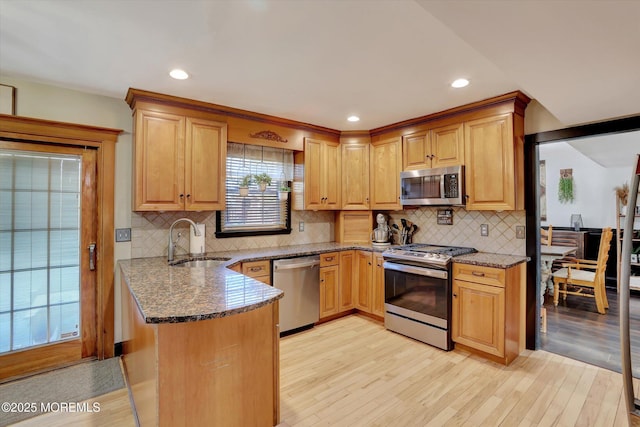 kitchen featuring sink, light hardwood / wood-style flooring, dark stone counters, kitchen peninsula, and stainless steel appliances