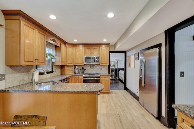 kitchen featuring sink, light stone counters, kitchen peninsula, stainless steel appliances, and light wood-type flooring