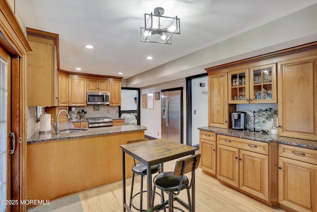 kitchen with stainless steel appliances, sink, light wood-type flooring, and dark stone counters