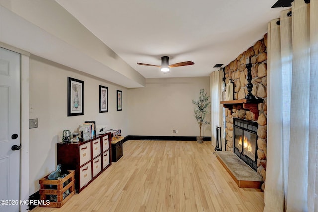 living room featuring a stone fireplace, ceiling fan, and light wood-type flooring