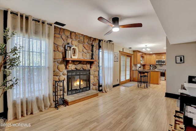 living room with a stone fireplace, light hardwood / wood-style floors, and ceiling fan