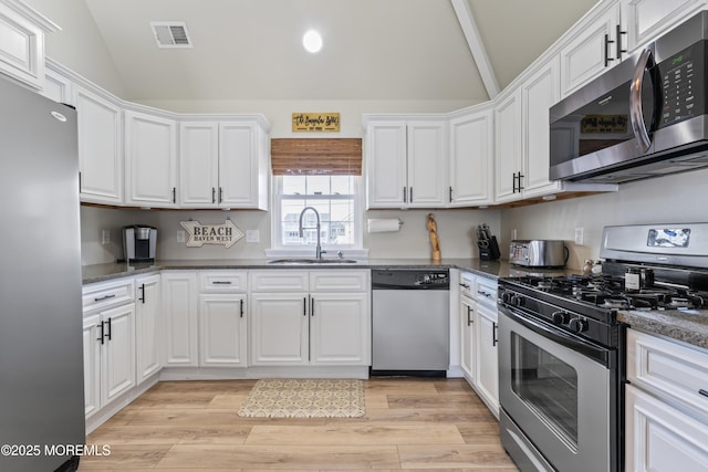 kitchen featuring sink, vaulted ceiling, light hardwood / wood-style flooring, appliances with stainless steel finishes, and white cabinets