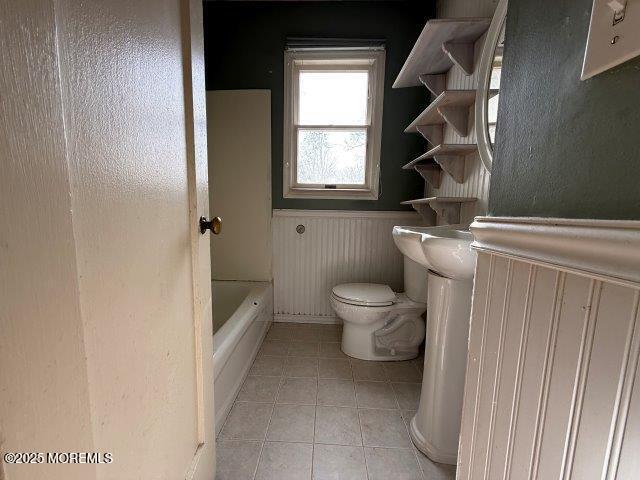 bathroom featuring tile patterned flooring, toilet, and a tub to relax in