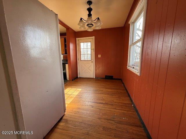 doorway with hardwood / wood-style flooring, an inviting chandelier, and wooden walls