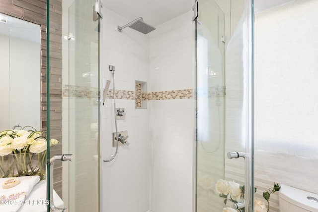 bathroom featuring a shower with door and toilet