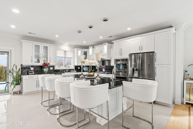 kitchen featuring an island with sink, a breakfast bar area, hanging light fixtures, stainless steel refrigerator with ice dispenser, and a healthy amount of sunlight