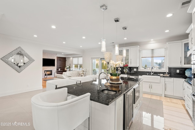 kitchen with pendant lighting, sink, white cabinetry, an island with sink, and dark stone counters