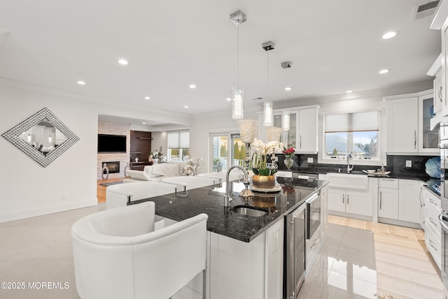 kitchen featuring sink, a kitchen island with sink, white cabinets, decorative light fixtures, and dark stone counters