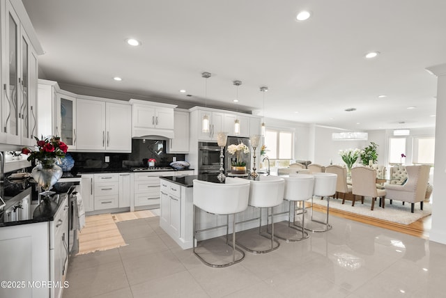 kitchen featuring pendant lighting, white cabinetry, an island with sink, and a kitchen bar