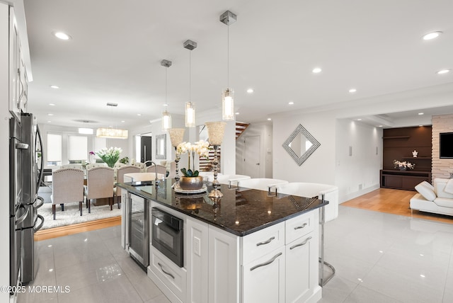 kitchen with a breakfast bar, white cabinetry, dark stone countertops, a center island, and decorative light fixtures