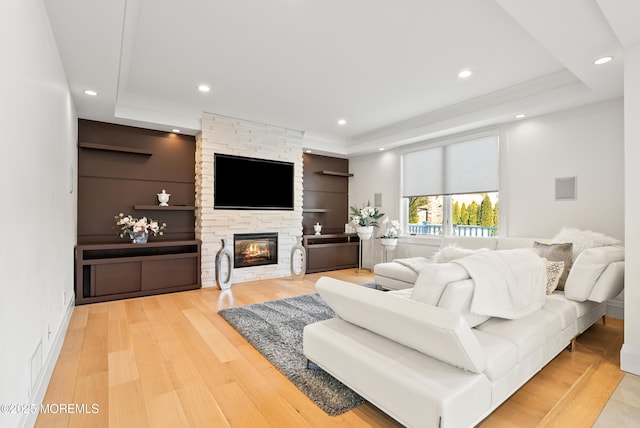 living room with hardwood / wood-style flooring, crown molding, a stone fireplace, and a tray ceiling