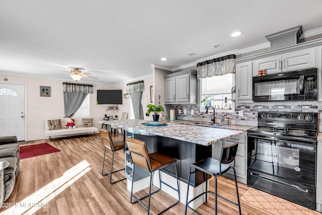 kitchen with tasteful backsplash, sink, a breakfast bar area, gray cabinetry, and black appliances