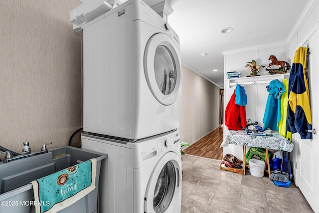 clothes washing area with stacked washer and dryer, ornamental molding, and sink