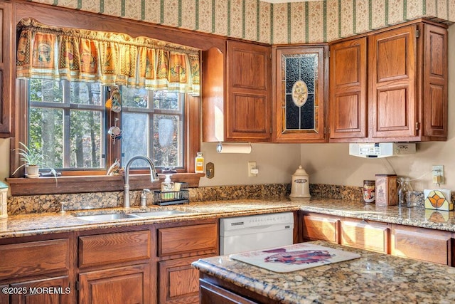 kitchen with white dishwasher, light stone countertops, and sink