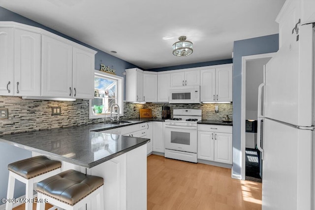 kitchen featuring sink, a breakfast bar area, white cabinetry, kitchen peninsula, and white appliances