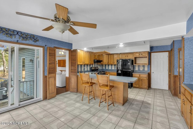 kitchen with a kitchen bar, black refrigerator with ice dispenser, stainless steel range, kitchen peninsula, and ceiling fan