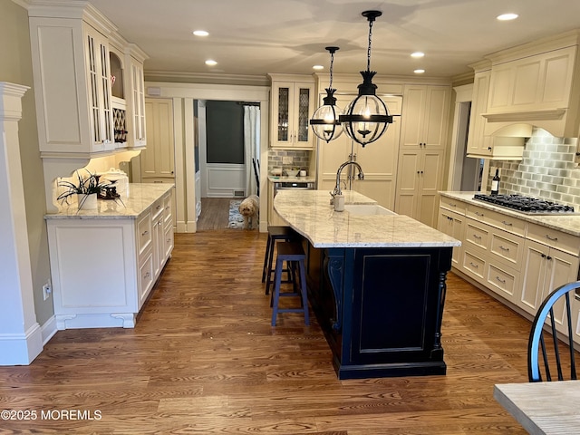 kitchen featuring decorative light fixtures, sink, stainless steel gas cooktop, light stone counters, and a center island with sink