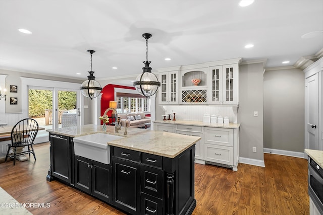 kitchen featuring sink, dark wood-type flooring, white cabinetry, hanging light fixtures, and a center island with sink