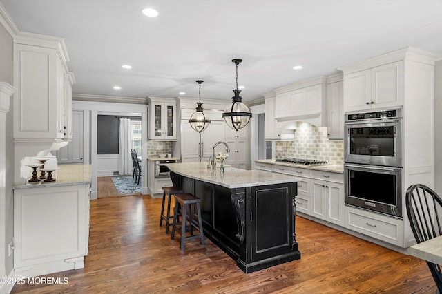 kitchen with light stone counters, stainless steel appliances, a kitchen island with sink, and white cabinets