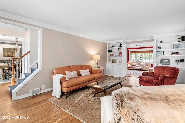 living room with a notable chandelier, crown molding, built in features, and hardwood / wood-style floors