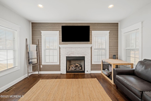 living room featuring a brick fireplace, dark hardwood / wood-style floors, and wood walls