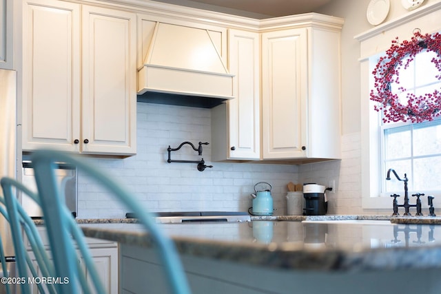 kitchen featuring premium range hood, decorative backsplash, and cream cabinetry