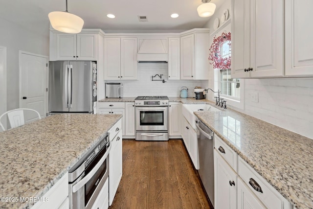 kitchen with pendant lighting, sink, stainless steel appliances, custom range hood, and white cabinets