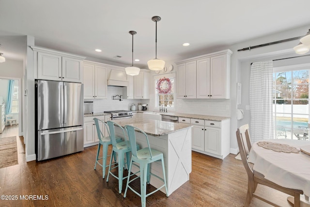 kitchen featuring a kitchen island, appliances with stainless steel finishes, pendant lighting, white cabinets, and light stone counters