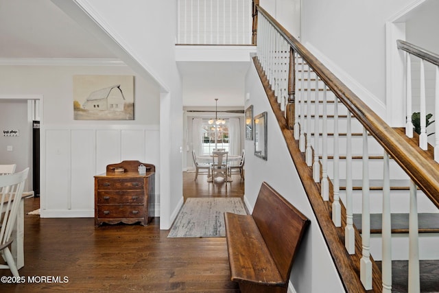 staircase featuring a high ceiling, ornamental molding, hardwood / wood-style floors, and a chandelier