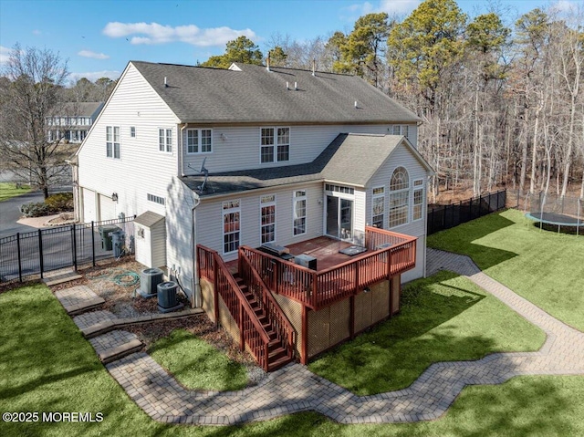 rear view of house featuring central AC unit, a wooden deck, a trampoline, and a lawn