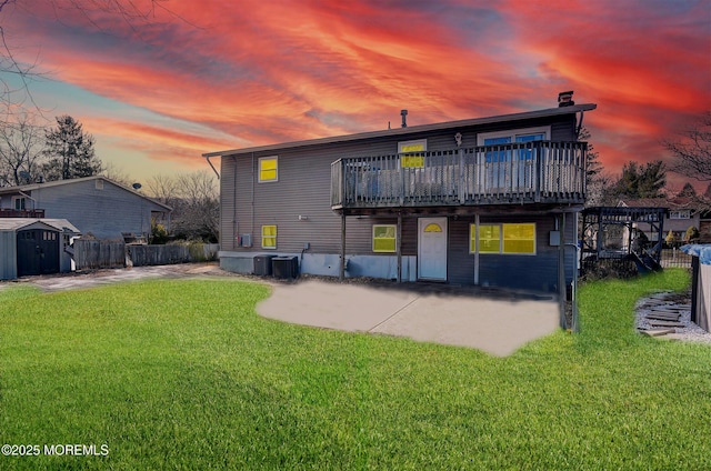 back house at dusk with a lawn, a storage unit, a patio area, and central air condition unit