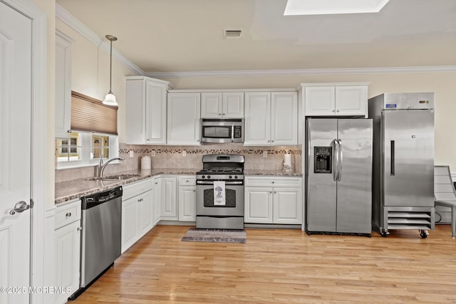 kitchen with pendant lighting, stainless steel appliances, white cabinets, a sink, and light stone countertops