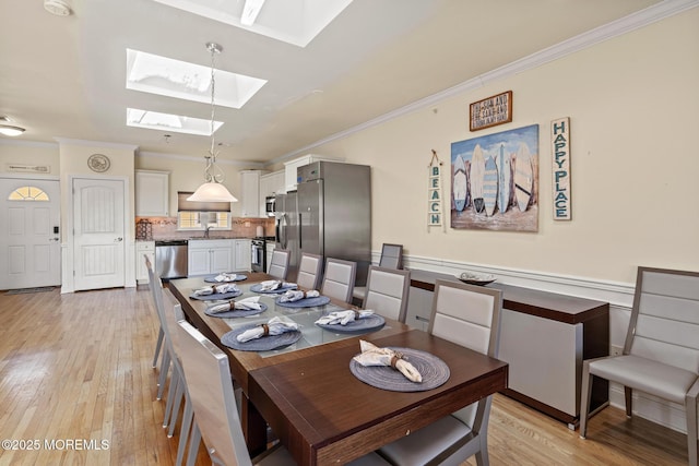 dining space with a skylight, crown molding, and light wood finished floors