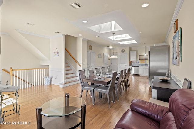 living area featuring a skylight, light wood finished floors, visible vents, stairs, and crown molding