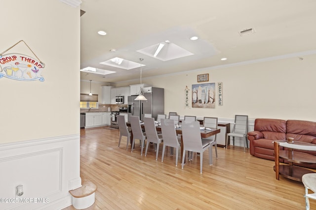 dining room with a skylight, crown molding, light wood finished floors, recessed lighting, and visible vents