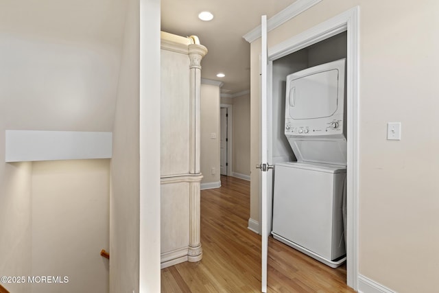 laundry area with laundry area, stacked washer / dryer, baseboards, ornamental molding, and light wood finished floors