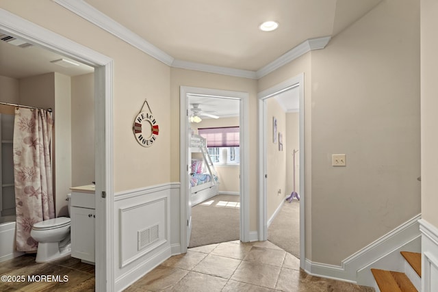 corridor featuring wainscoting, crown molding, visible vents, and stairs